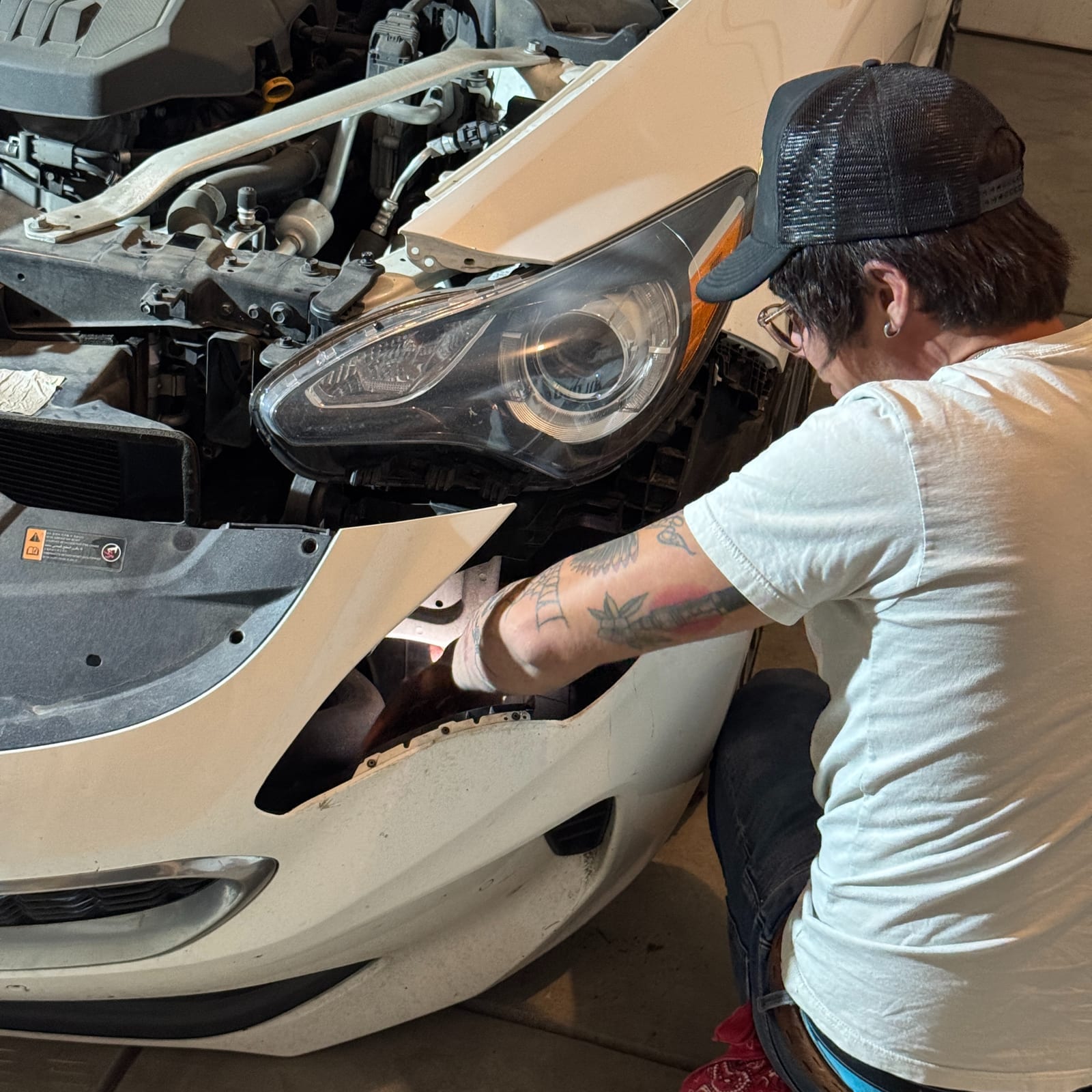 Technician working on a car's front end with the bumper cover removed